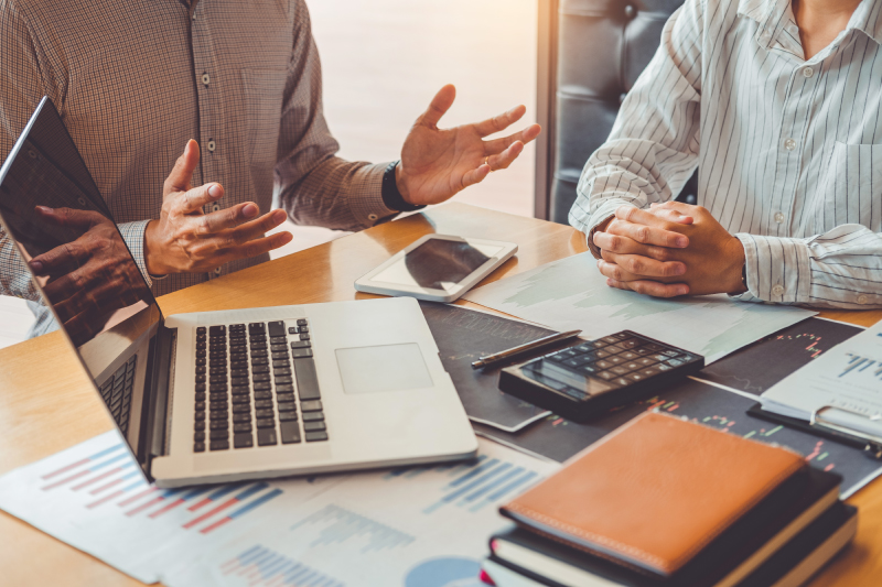 売上グラフやマーケティング資料を前に、クライアントと提案内容を話し合う様子